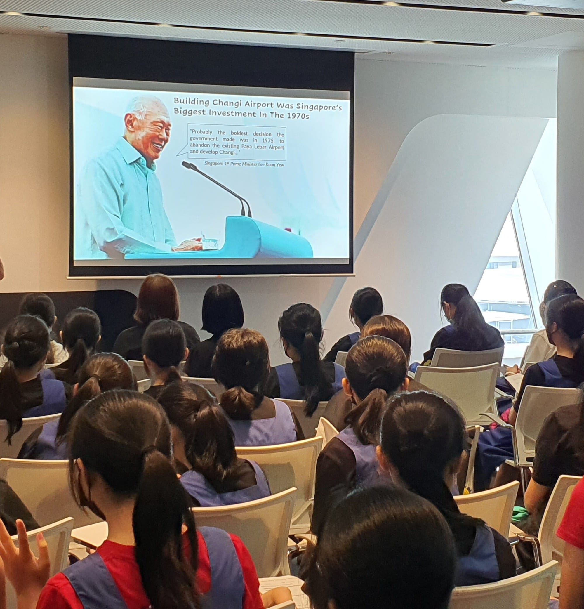 Audience seated in a room watching a presentation slide about building Changi Airport being Singapore's biggest 1970s investment.